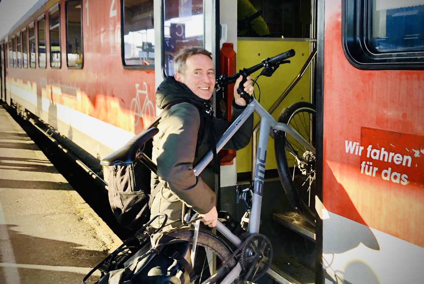 Markus Büchler steigt mit grauen Fahrrad über zwei Stufen in roten Regiozug.