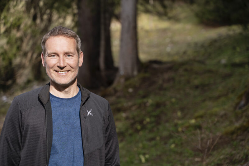 Dr. Markus Büchler Porträt, im Hintergrund ein Berghang mit Nadelbäumen